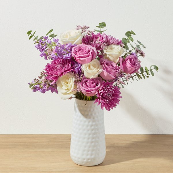 Fildişi ve mor güllerden oluşan, pembe krizantemlerle süslenmiş bir buket aranjman