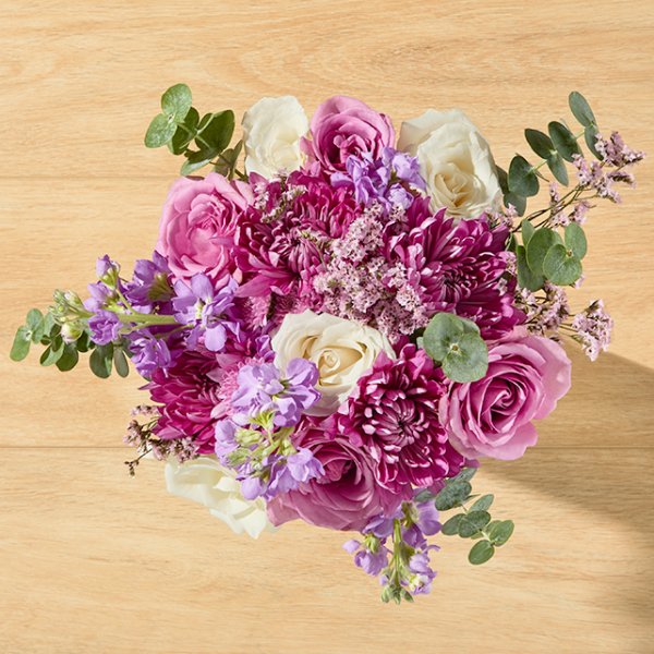 Fildişi ve mor güllerden oluşan, pembe krizantemlerle süslenmiş bir buket aranjman